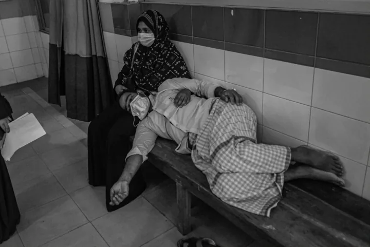 A man rests his head on a woman’s lap on a hospital bench.