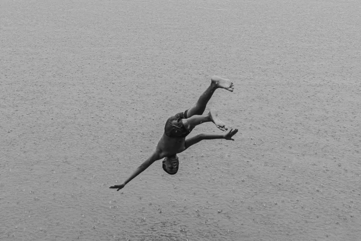 A person twists in midair above water in a black-and-white photograph.
