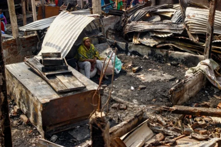 A woman sits among scorched timber and collapsed corrugated metal sheets.