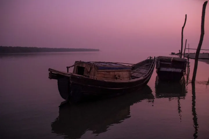Wooden boats and their reflections rest on calm water beneath a purple-pink sky.