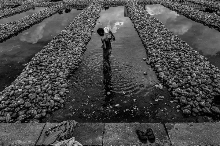 A man pours water over his shoulder while standing in a narrow pool between rows of stones.