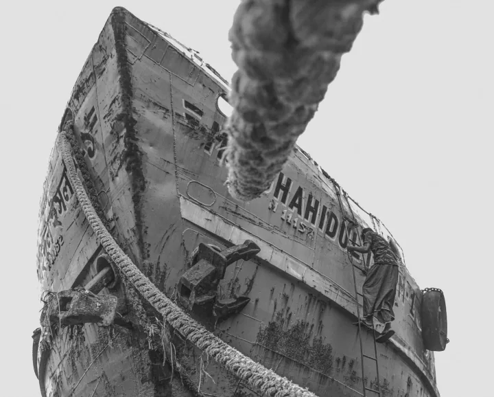 A low-angle black-and-white view of a weathered boat’s bow and thick mooring rope.
