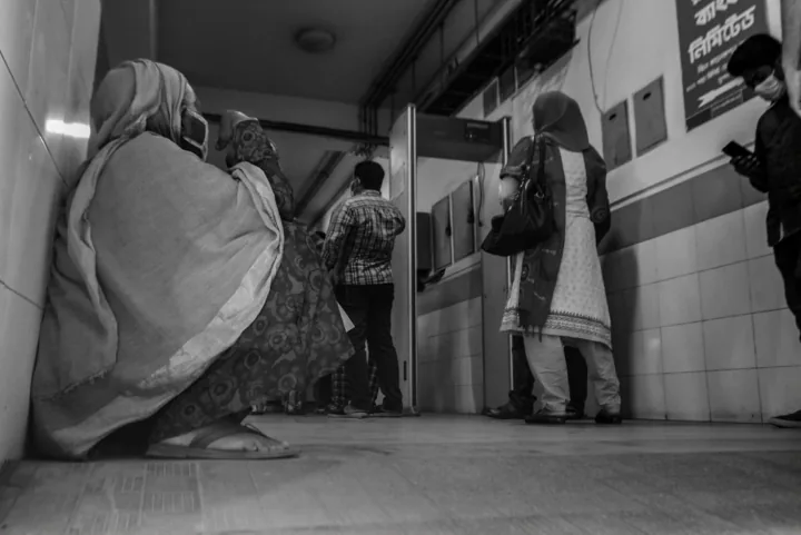 People wait along a hospital corridor, with a seated woman in the foreground.