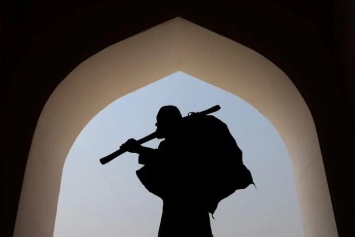 A worker carrying a bundle and a pole is silhouetted inside a mosque arch.