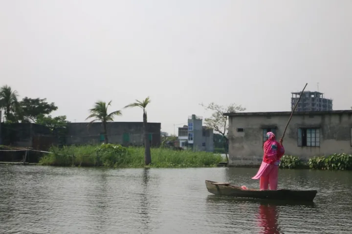 A woman in pink stands in a narrow wooden boat and poles across floodwater.