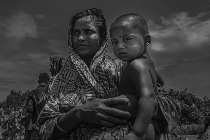 A mother holds a young child against her shoulder outdoors.