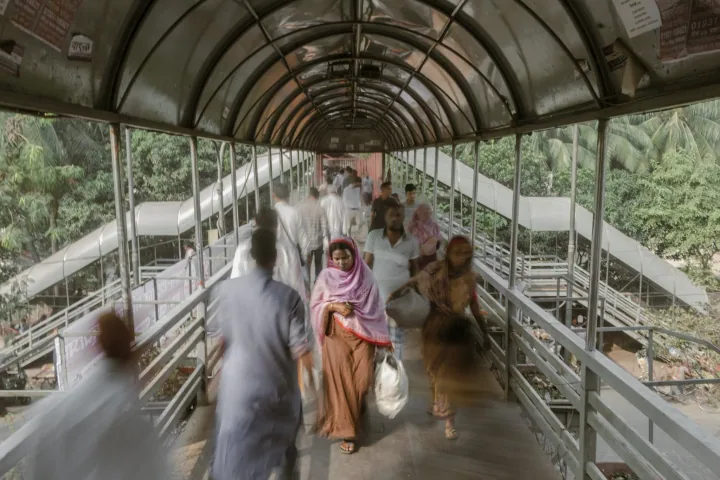 People walk through an arched, covered footbridge, some blurred in motion around a woman in pink.