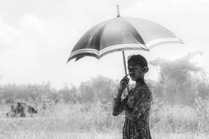 A girl stands beneath a large umbrella in an open field.