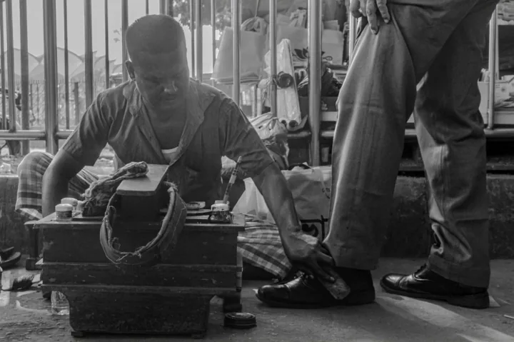 A shoeshiner brushes a customer’s shoe beside his wooden work box.
