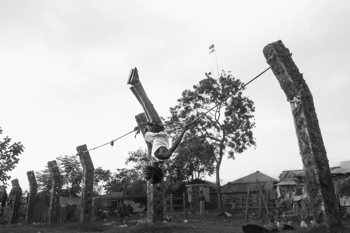 A child hangs upside down from a rope stretched between wooden posts.