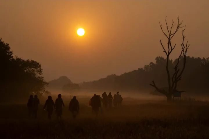 People walk through misty fields beneath an orange winter sunrise.